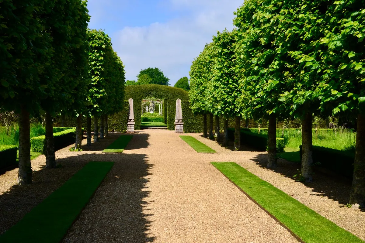 Baumgesäumter Gartenweg mit Kiesbelag und Hecken