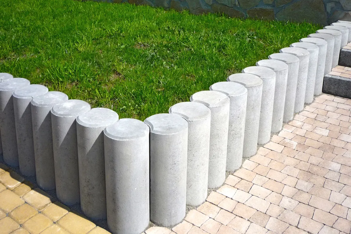 Weiße Betonpalisaden als Randeinfassung am Rasen